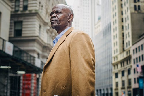 Serious black businessman between urban multistory buildings