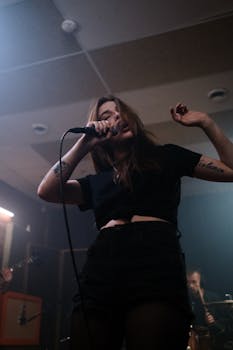 Capture of a tattooed female singer passionately performing with a microphone indoors.