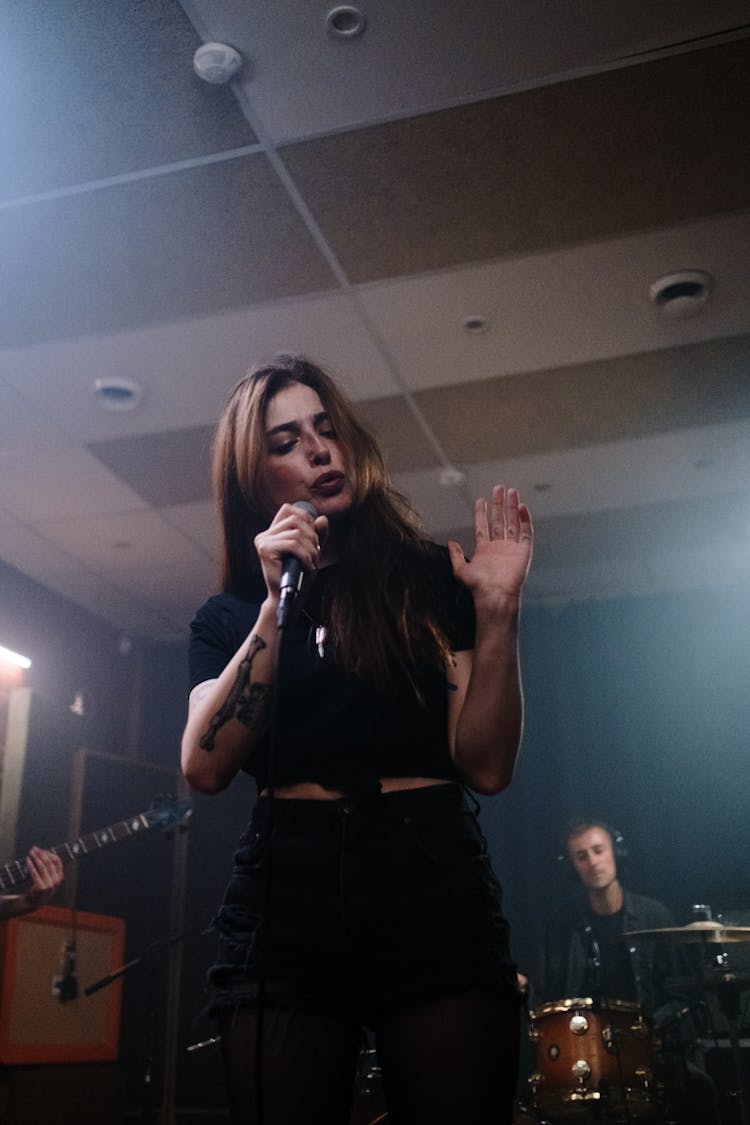 Woman In Black Tank Top And Black Denim Jeans Singing With Microphone