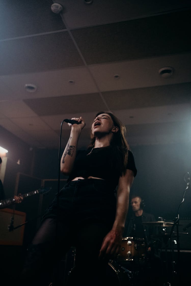 Woman In Black Clothes Holding Microphone While Singing 