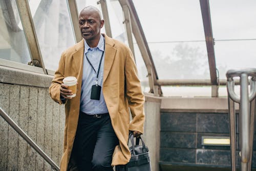 Pondering black male manager with coffee to go on stairs