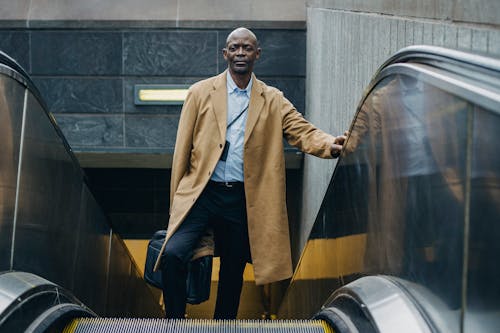 Serious black male office worker on escalator in town