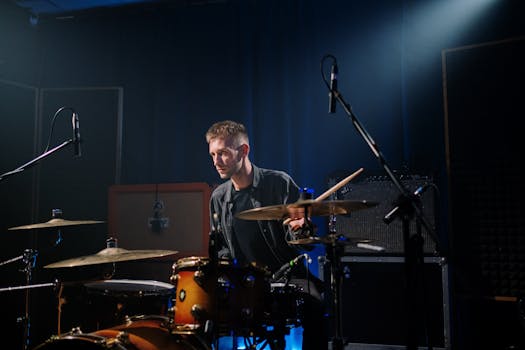 A male drummer intensely performing during a live stage performance under spotlight.