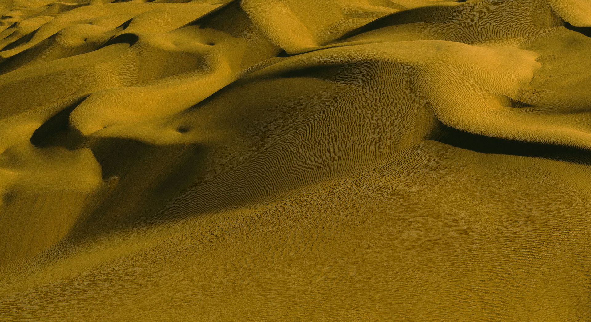 Aerial view of golden sand dunes with intricate patterns in the Xinjiang desert, China.