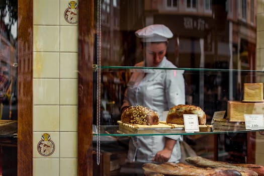 Chef behind a bakery window showcasing gourmet breads on glass shelves.