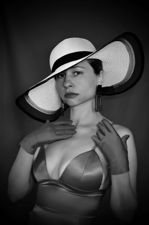 Black and white of charming woman in stylish outfit and hat looking at camera against fabric background