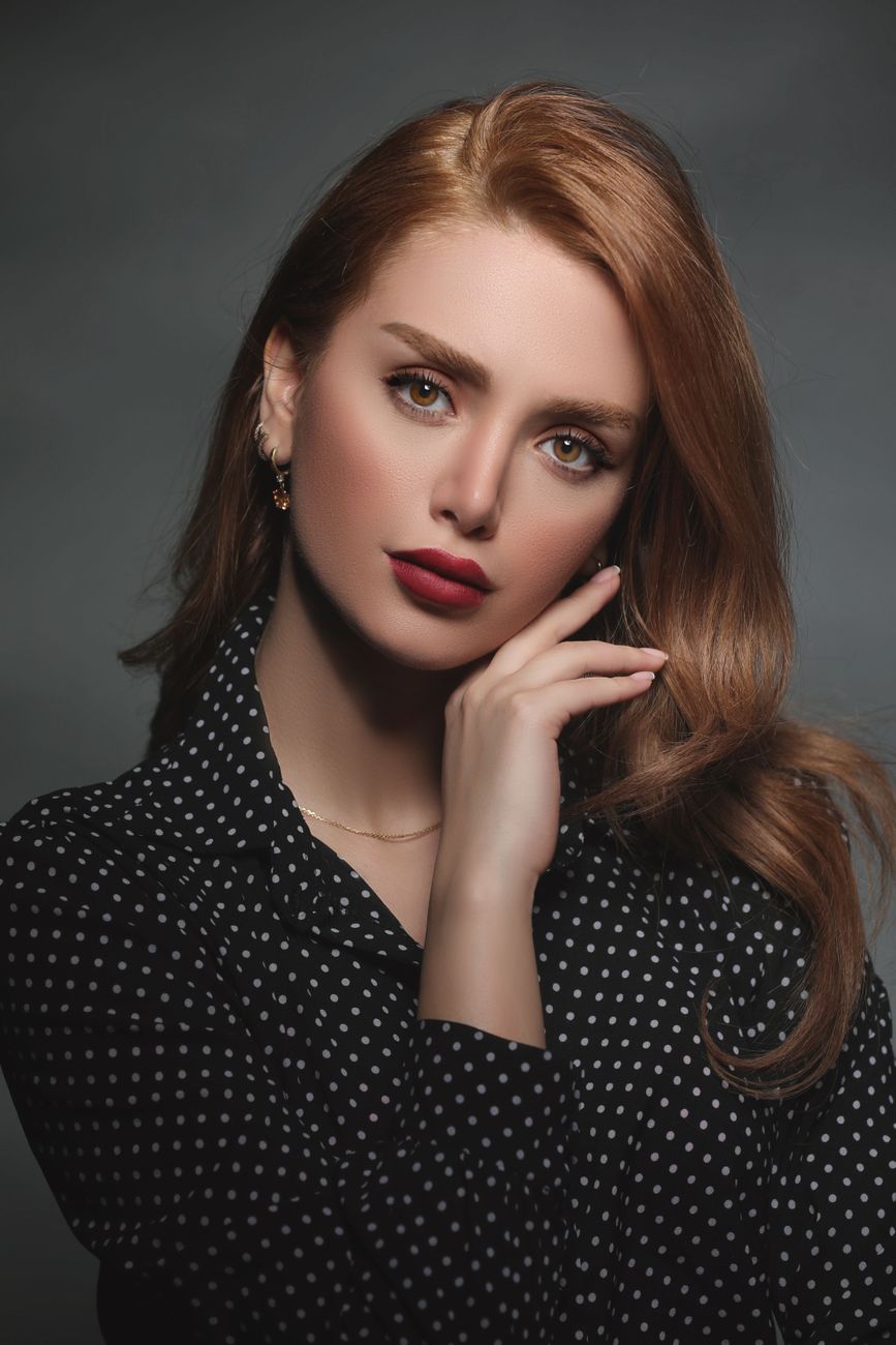 Studio portrait of a woman with long hair and brown eyes in a polka dot blouse, elegantly posed.
