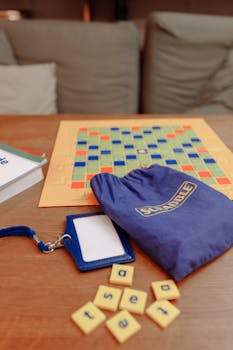 Close-up of a Scrabble board game setup with tiles and bag on a wooden table.