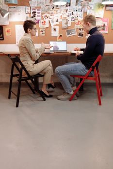 Two adults in a brainstorming session with a laptop in an office.