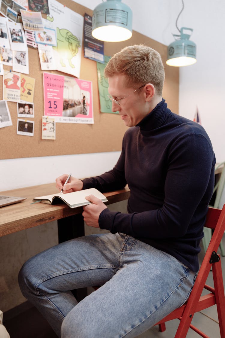 A Man Smiling While Writing On A Notebook 