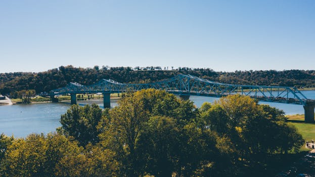 A picturesque view of a blue truss bridge over a serene river with lush greenery.