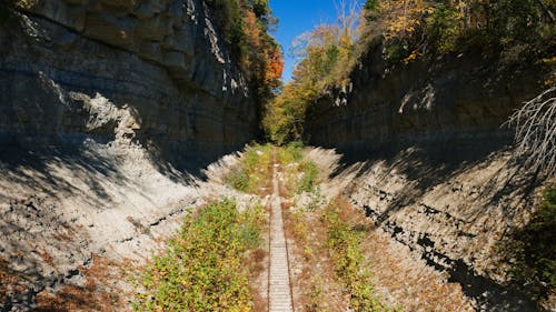 Perspective view of rural railway running through rough rocky ravine in mountainous terrain on sunny summer day