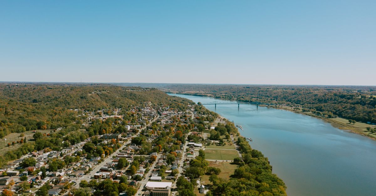 Drone view of small tranquil town located on vast azure river coast on sunny summer day