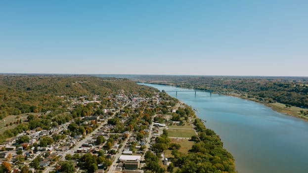 Aerial view of a tranquil riverside town with lush greenery and clear blue skies.