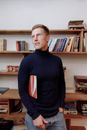 Man in Black Turtleneck Sweater Standing Beside Brown Wooden Shelf