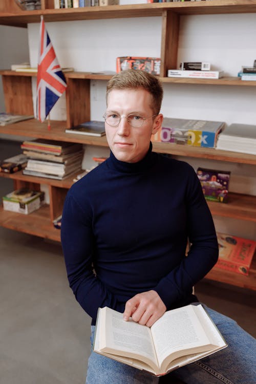 Man in Black Sweater Wearing Eyeglasses while Holding a Book