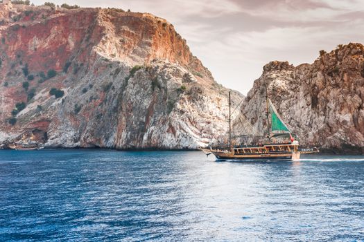 A sailing ship navigates the serene waters near towering rocky cliffs, capturing the essence of adventure.
