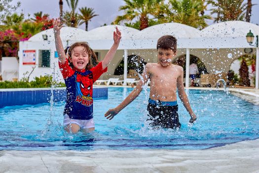 Two kids enjoying a fun day playing and splashing in an outdoor swimming pool.