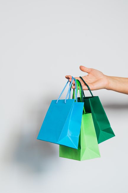 Hand holding three colorful paper shopping bags on a white b