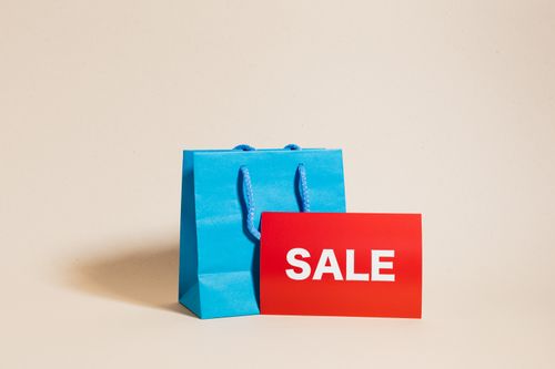 Free Blue shopping bag with red sale sign on neutral background, ideal for promotions. Stock Photo