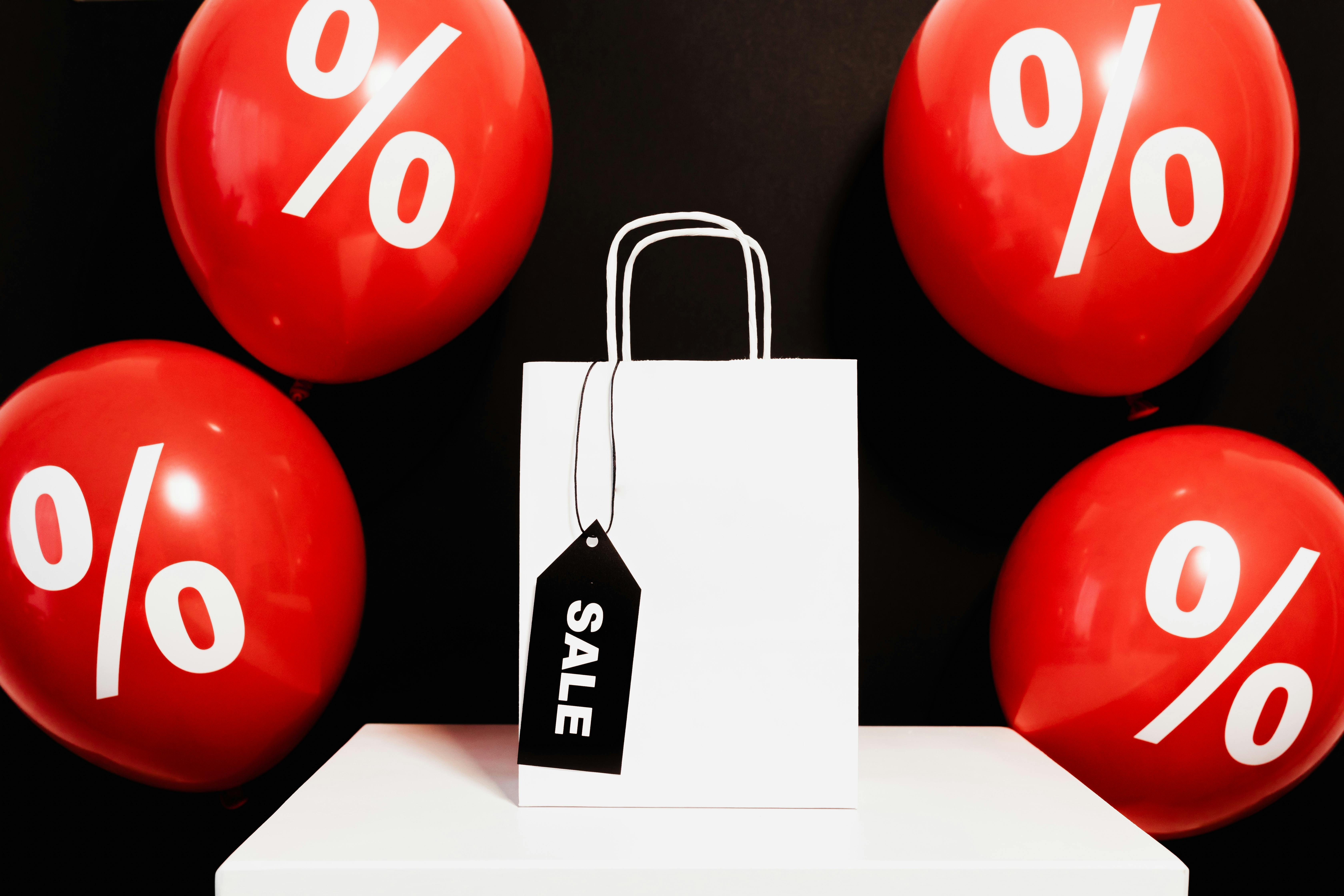 white paper bag surrounded by red balloons