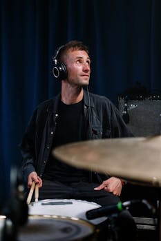 A male drummer immersed in his music, playing the drum set with headphones on in a sound studio.