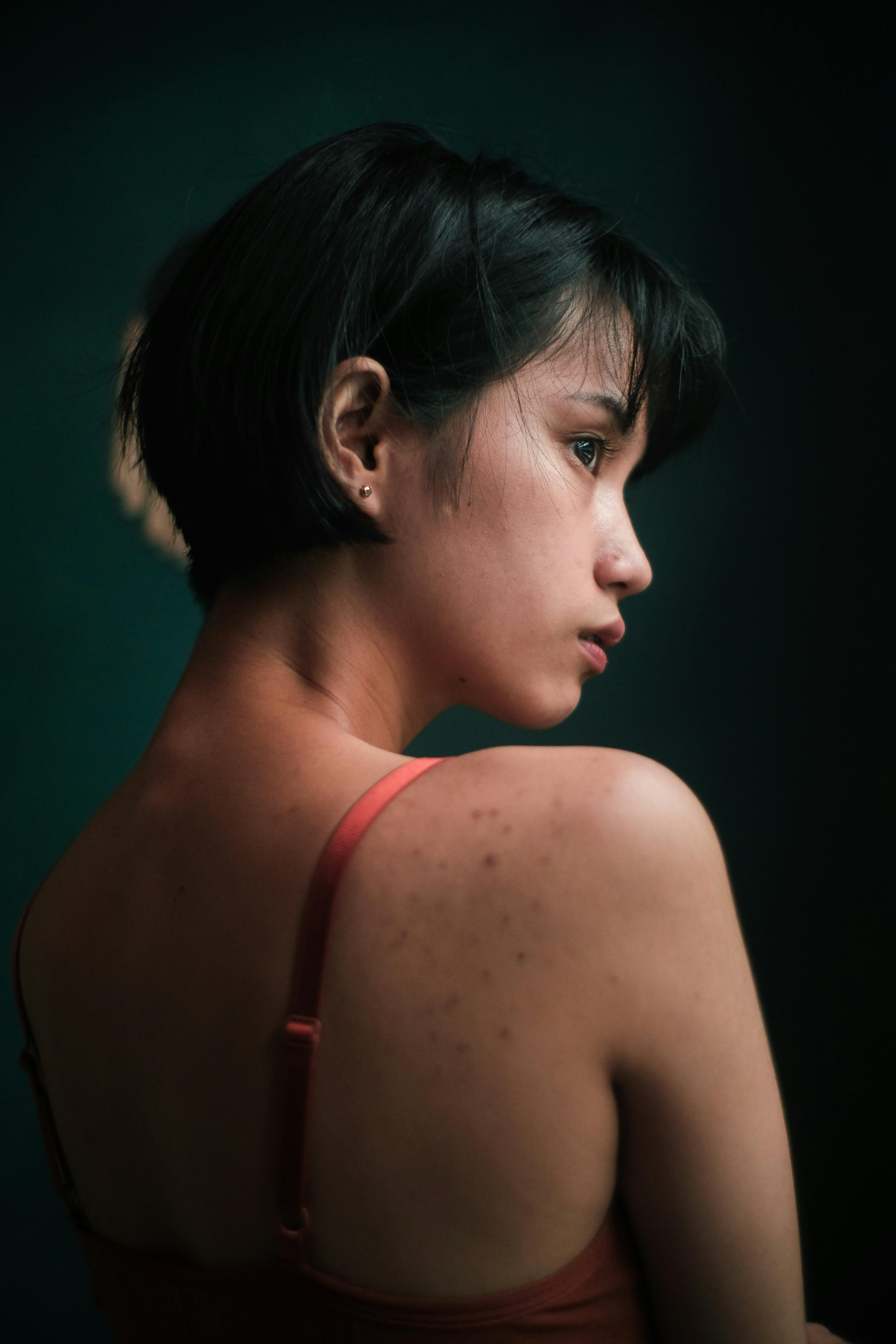 Thoughtful  young woman with short dark hair standing in dark room and looking away