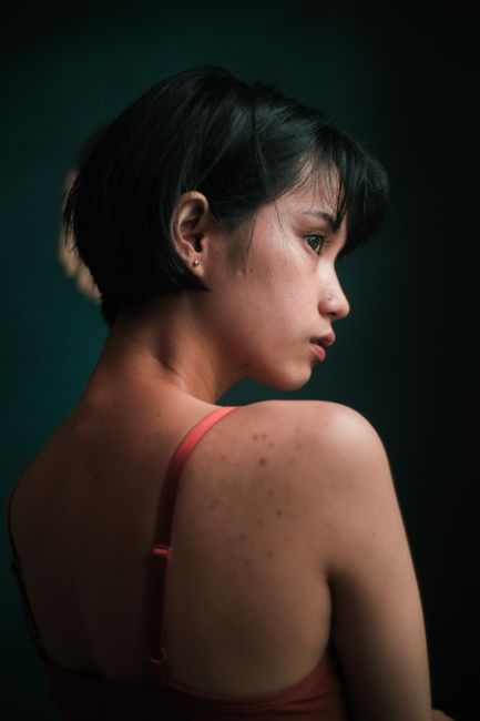 Thoughtful young woman with short dark hair standing in dark room and looking away