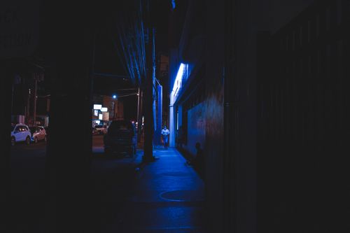 Free A person walks along a dimly lit street at night, illuminated by neon blue lights. Stock Photo