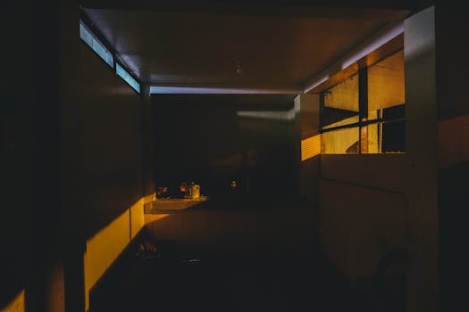 Dimly lit kitchen interior with dramatic lighting casting shadows, creating a moody atmosphere.