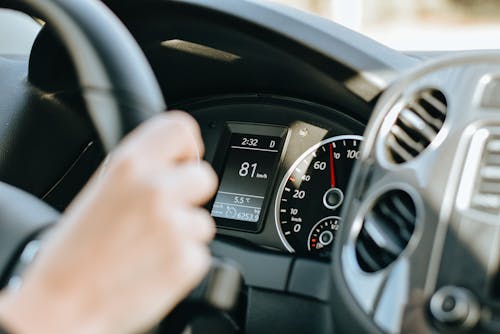 Crop anonymous person holding black steering wheel and driving car in sunny day