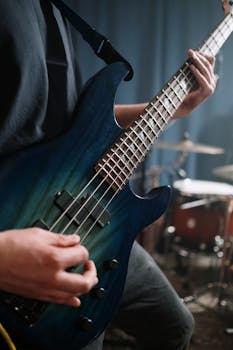Detailed view of a musician playing a blue bass guitar in a sound studio, showcasing musical performance.