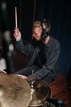 A drummer in a studio playing drums with focus, wearing headphones. Vertical shot.