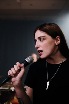 Caucasian woman passionately singing into a microphone in a music studio setting.