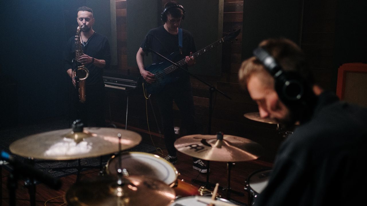 Musicians rehearse together with several instruments, including drums, saxophone and bass.