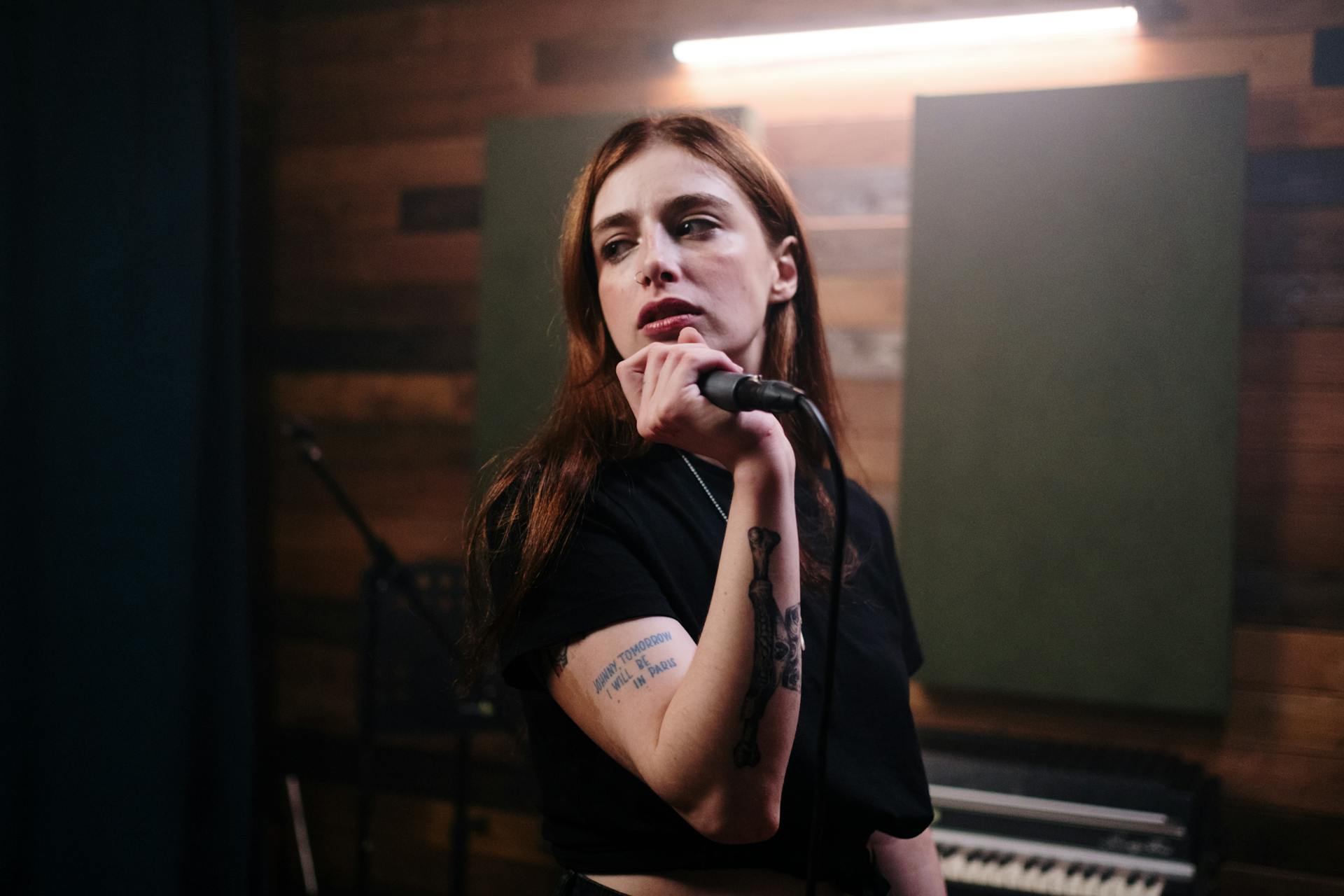 Tattooed artist performing with microphone in music studio.