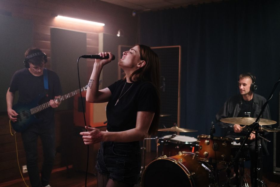 A vibrant indie music band rehearsing indoors with a singer, guitarist, and drummer.