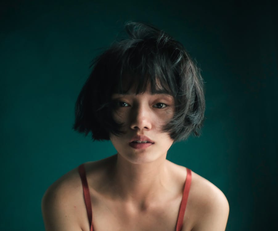 Sad Asian female with short disheveled hair and brown eyes looking at camera against blurred background