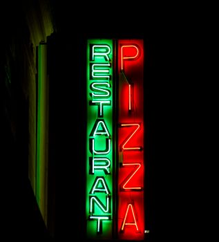 Colorful neon sign for pizza restaurant illuminating a Paris night scene.