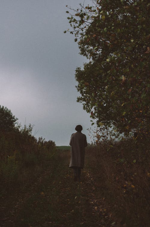 Back View of Person in Overcoat Walking on Grass Field 