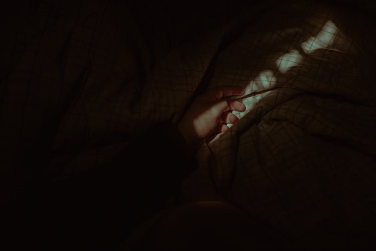 Crop Unrecognizable Person Hand Lying On Comfy Blanket In Darkness