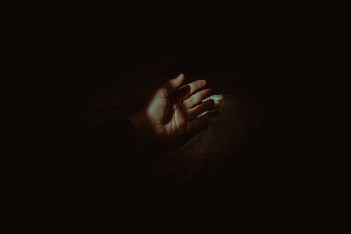 Free Crop anonymous person hand lying on cozy soft bed in dark bedroom with beam of light Stock Photo