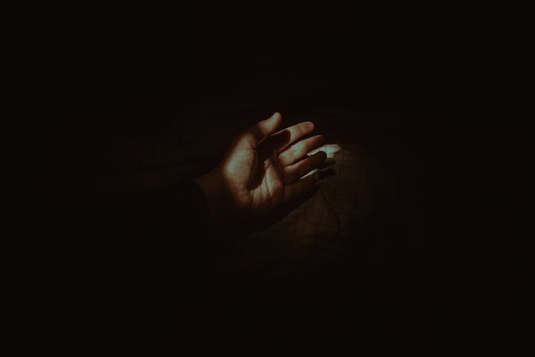 Crop Faceless Person Hand Lying On Comfy Bed In Darkness