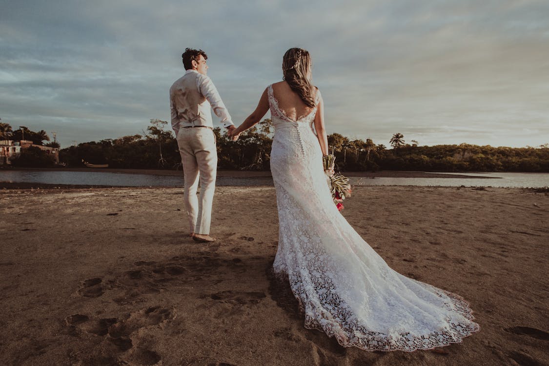 Free Bride and groom walking on sandy coastline Stock Photo