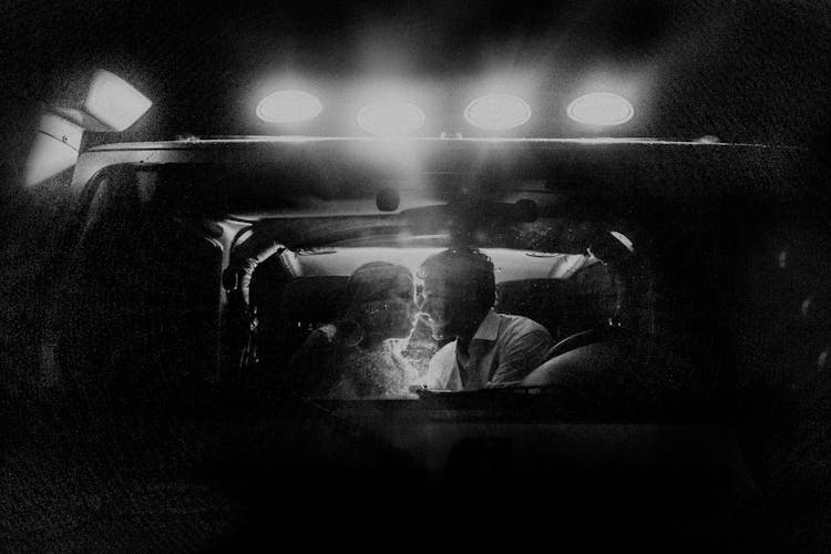 Couple Sitting In Front Seat Of Car In Spotlight