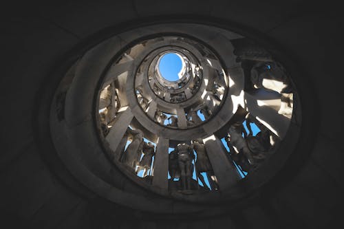 From below of spiral shaped aged house interior with assorted masonry statues under blue sky