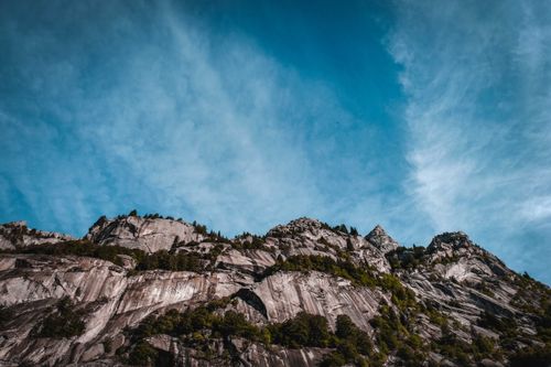 Free Low angle scenic view of high vertical mountain with growing green trees under blue sky with fluffy clouds Stock Photo