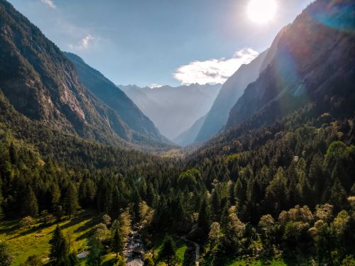 Free Spectacular view of valley with lush trees between high mounts under cloudy sky with glowing sun Stock Photo