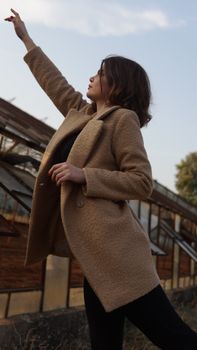 Stylish woman in a warm coat pointing upwards in an outdoor setting.