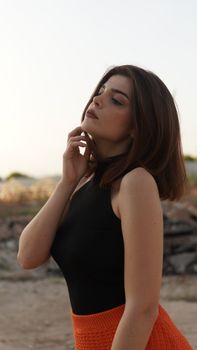 Elegant brunette woman posing outdoors in a stylish black and orange outfit.